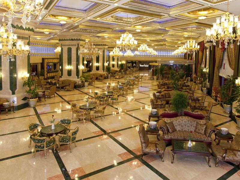 Velká luxusní hotelová hala s křesly, stolky a elegantními lustry.