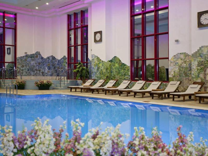 Vnitřní bazén s lehátky a horskou malbou za fialového osvětlení.