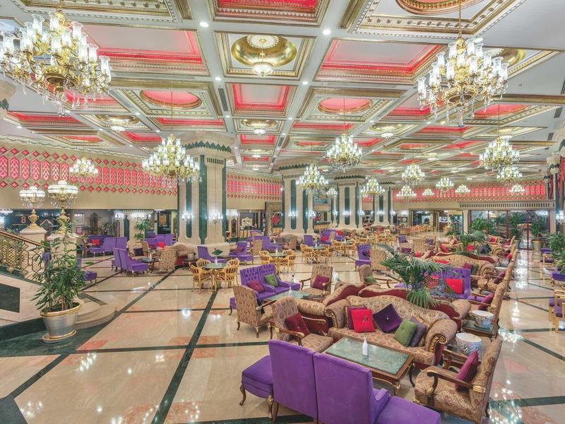 Prostorná hala luxusního hotelu s fialovými sedacími soupravami, elegantními lustry a lesklou mramorovou podlahou.