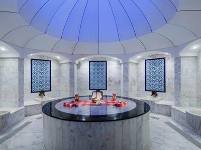Elegante hammam met mozaïekmuren, ronde vijver en koepelvormig plafond in zachte blauwe tinten.