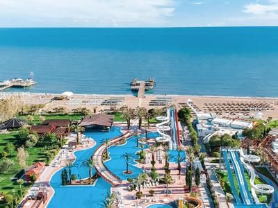 Breed hotelzwembad met glijbanen en ligstoelen op het strand naast de zee.