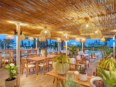 Espace de restaurant ouvert avec mobilier en bois et plantes sous une structure de plafond en bois.