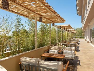 Terrasse avec toits en bois et chaises rembourrées devant un hôtel avec vue sur des plantes vertes.