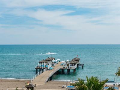 Longue jetée en bois s'étendant de la plage à la mer sous un ciel bleu avec des nuages.