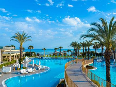 Basen hotelowy z palmami i leżakami pod błękitnym niebem nad morzem