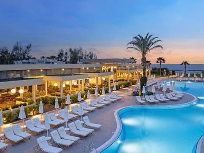 Espace piscine d'hôtel en soirée avec transats éclairés et palmiers sous un ciel bleu.