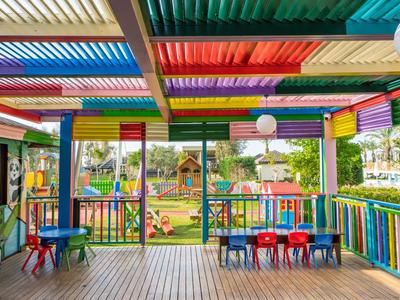 Kleurrijk overdekt buitengebied met kindertafels en uitzicht op een speeltuin.