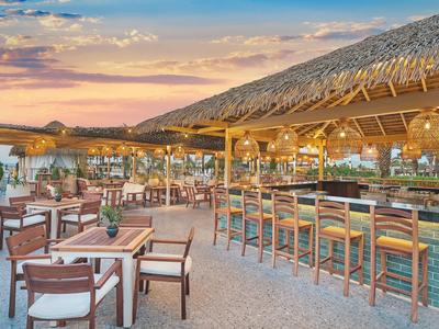 Otwarty bar na plaży z drewnianymi belkami, krzesłami i stołami o zachodzie słońca.