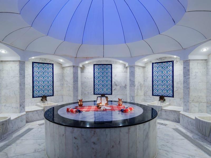 Elegante hammam met mozaïekmuren, ronde vijver en koepelvormig plafond in zachte blauwe tinten.