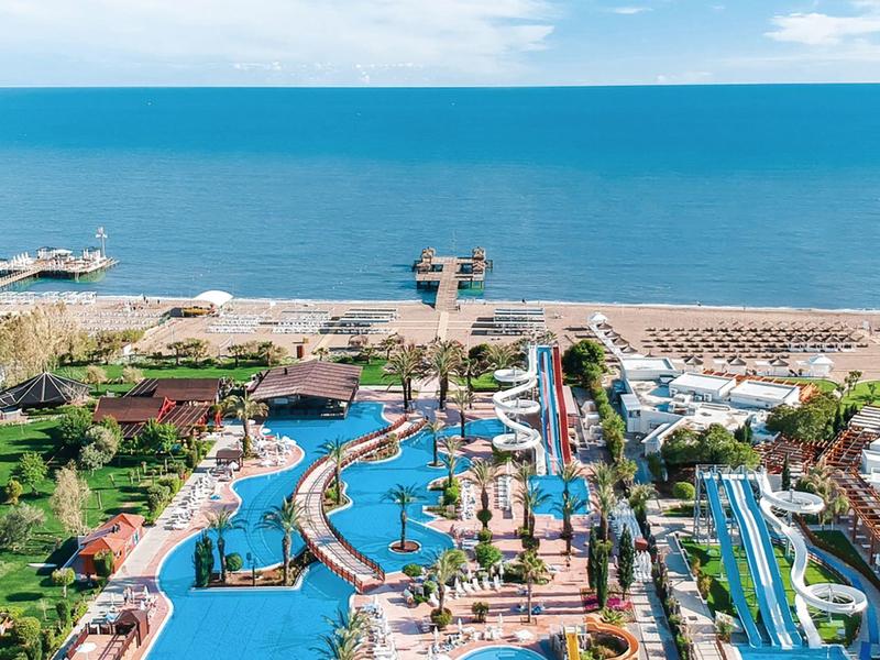 Breed hotelzwembad met glijbanen en ligstoelen op het strand naast de zee.