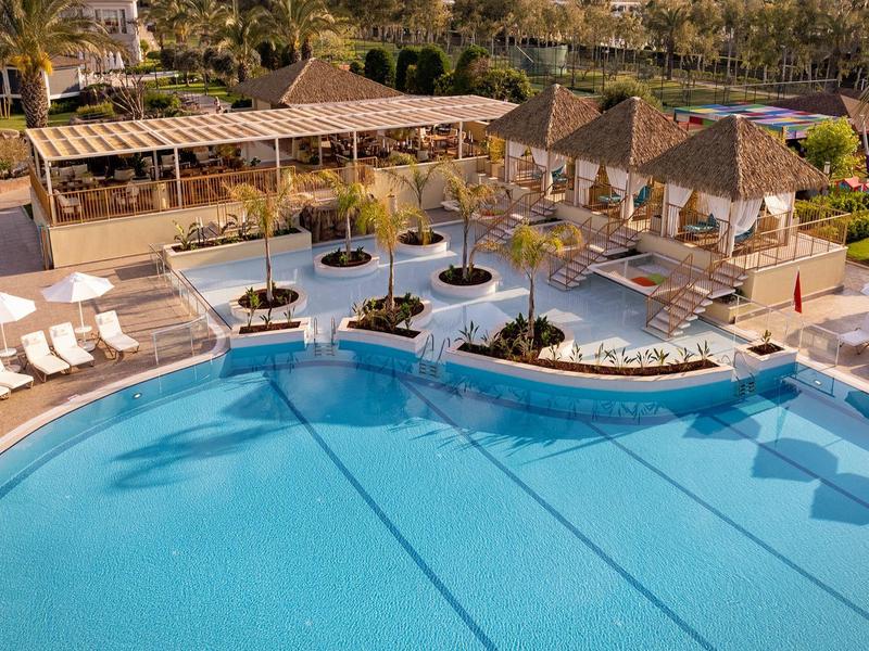 Grand piscine d'hôtel avec parasols, chaises longues et espaces de jardin environnants.