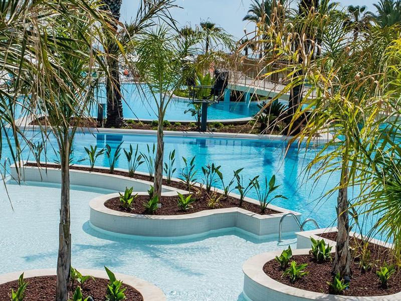 Piscine avec petites îles et palmiers dans une eau claire sous un ciel bleu.