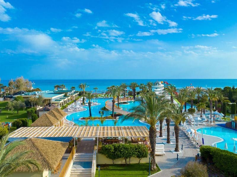 Uitzicht op een hotelresort met zwembad, palmbomen en directe toegang tot zee onder een blauwe lucht.