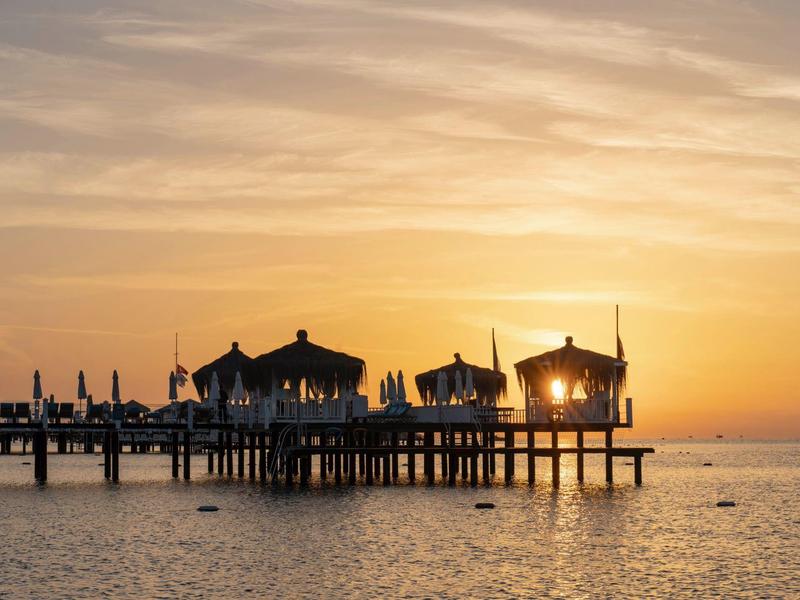 Jetée en bois avec pavillons au coucher du soleil sur une mer calme.