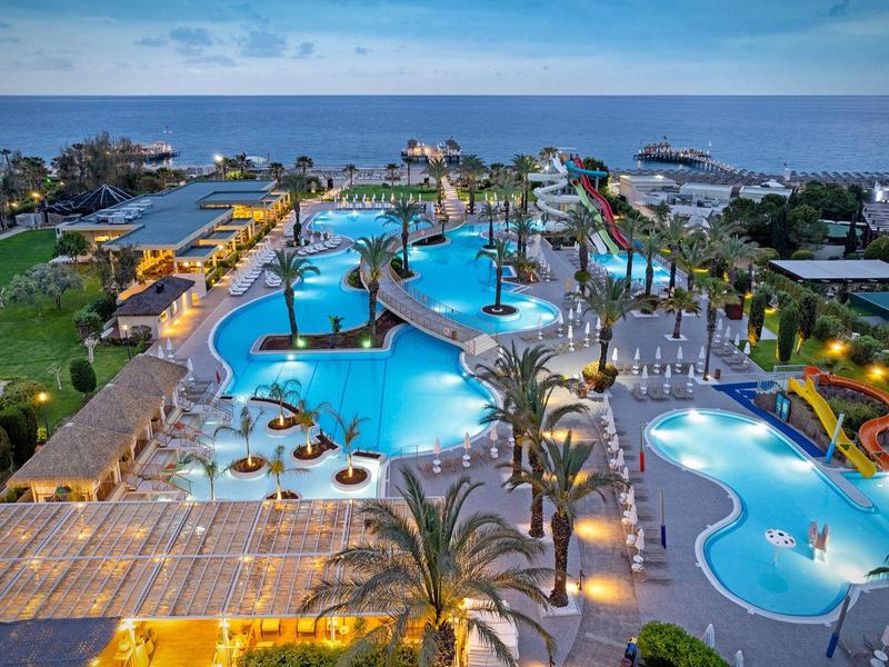 Groot hotelcomplex met meerdere verlichte zwembaden, glijbanen en palmbomen aan zee
