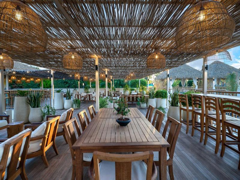 Terrasse extérieure confortable avec chaises et table en bois sous un toit en bambou avec lanternes.