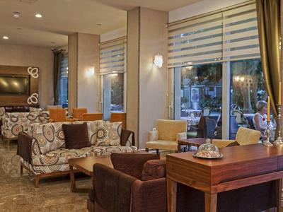 Gemütlicher Wohnbereich mit Sesseln, Sofas, Holztischen, großen Fenstern und warmem Licht.