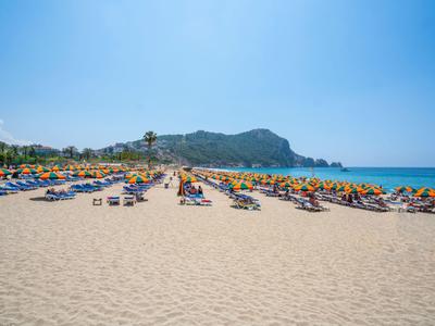 Breed zandstrand met ligstoelen en parasols naast helderblauwe zee en bergen op de achtergrond