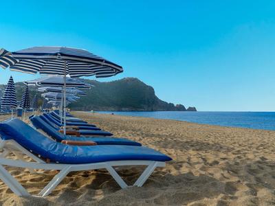 Lege ligstoelen met parasols op zandstrand onder een heldere blauwe lucht.