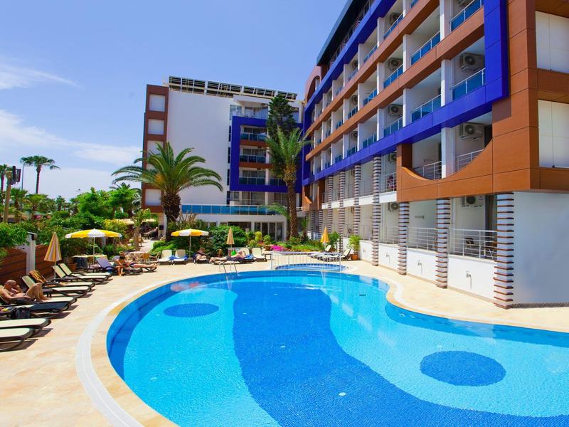 Moderner Hotelpool mit blauer Umrandung, Liegestühlen und Palmen bei sonnigem Wetter.