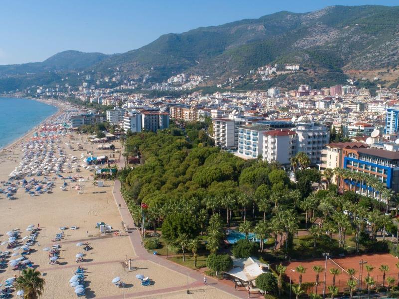 Langer Sandstrand mit Sonnenschirmen, dahinter dichte Stadt und bewaldete Hügel bei blauem Himmel.