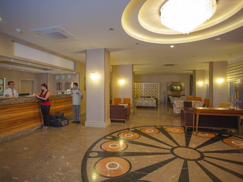 Hotelrezeption mit Empfangstresen, Rezeptionisten und einem Gast mit Koffer im hellen Eingangsbereich.