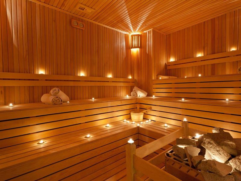 Sauna aus hellem Holz mit mehrstufigen Sitzbänken und vielen Kerzen für stimmungsvolle Beleuchtung.