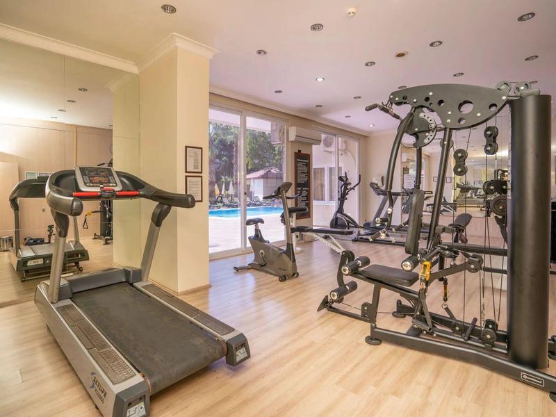 Helles Fitnessstudio mit Holzboden, Laufband, Kraftstation und großem Spiegel an der Wand.