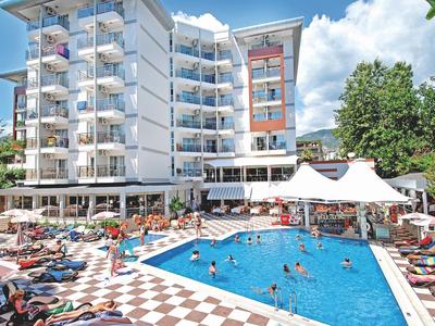 Moderner Hotelkomplex mit Außenpool, Liegestühlen und weißen Schirmen bei sonnigem Wetter.