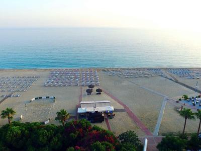Strand mit vielen Sonnenschirmen, Palmen und einem kleinen Gebäude am Meer bei Sonnenuntergang.