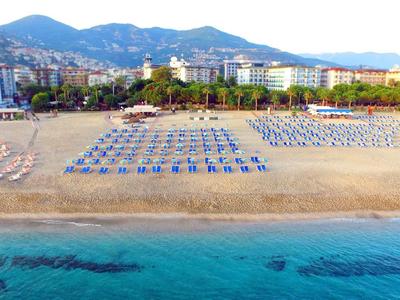 Spiaggia con lettini e hotel sullo sfondo lungo una costa con montagne.