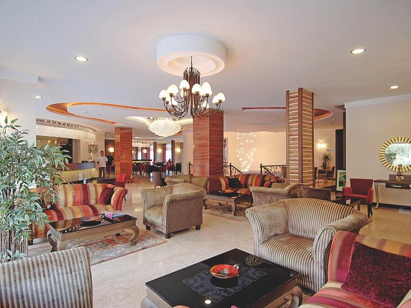 Großer Hotel-Lobbybereich mit bequemen Sesseln, Sofas, Pflanzen und dekorativen Lampen in warmen Farben.