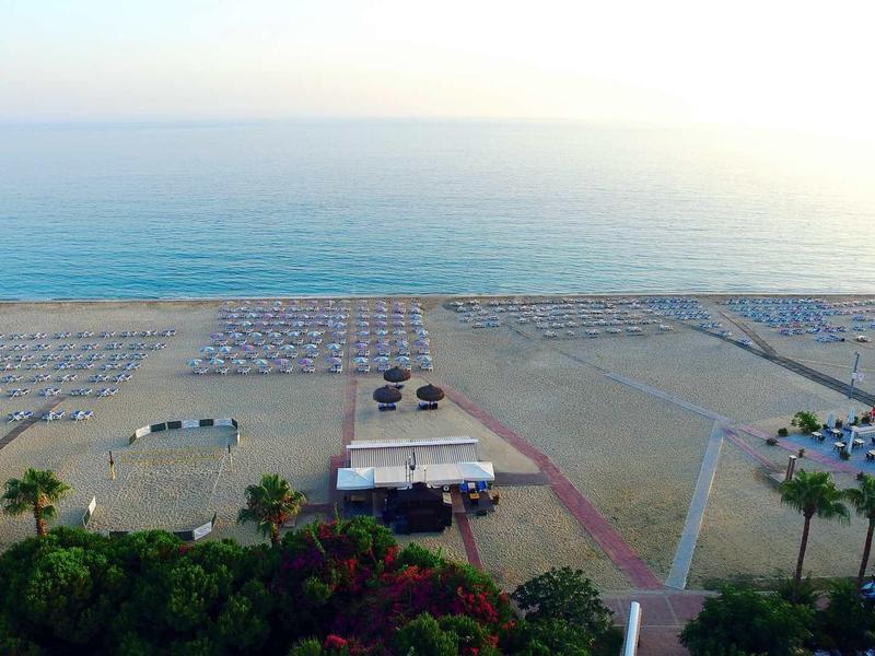 Strand mit vielen Sonnenschirmen, Palmen und einem kleinen Gebäude am Meer bei Sonnenuntergang.