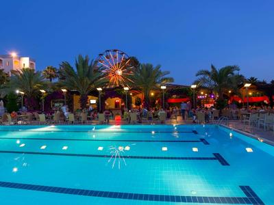 Piscina dell'hotel illuminata di notte con palme e una ruota panoramica sullo sfondo.