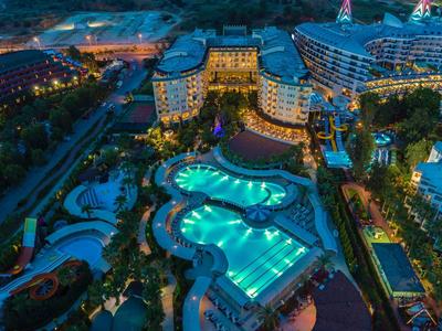 Noční pohled na osvětlené letovisko s několika bazény a okolními budovami.