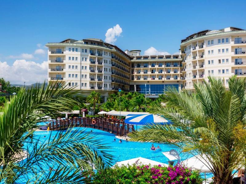 Velký hotel s venkovním bazénem a tropickými rostlinami za slunečného počasí.