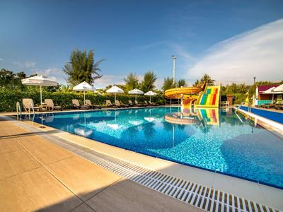 Großer Pool mit blauer Folie, Wasserrutsche, weißen Sonnenschirmen und grüner Umgebung.