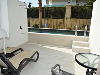 Moderner Außenbereich mit Pool, zwei Liegestühlen, kleinem Glastisch und Treppe zum Wasser.