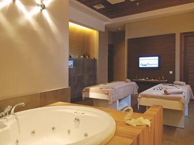 Ein gemütlicher Wellnessraum mit Whirlpool-Badewanne, zwei Massageliegen und warmem Licht.