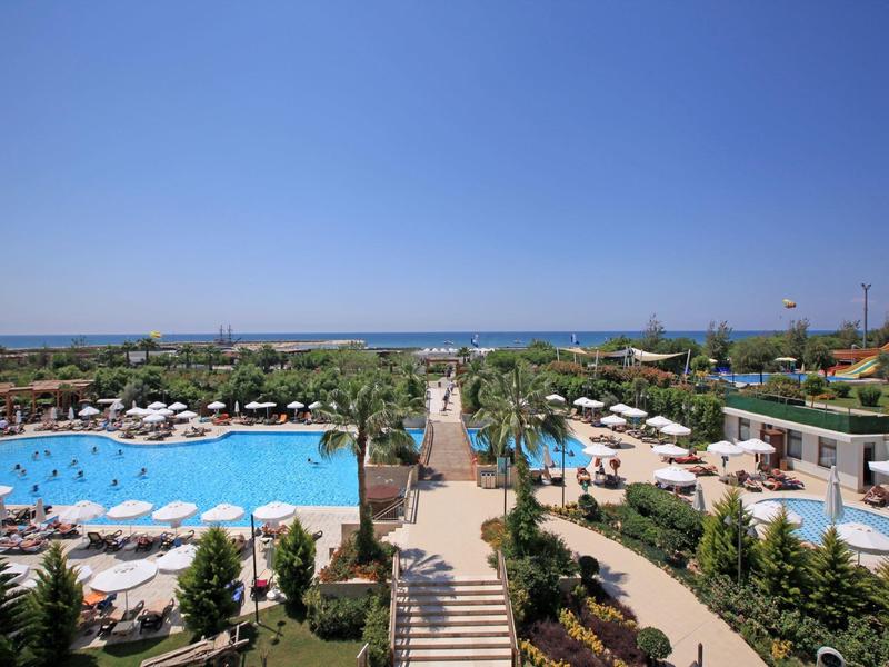 Resort zwembad met ligbedden, parasols, palmbomen en uitzicht op de oceaan onder een heldere hemel.
