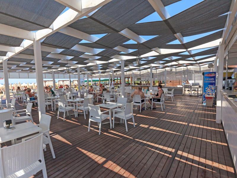 Ruim buitenterras met witte tafels en stoelen onder een moderne luifel.