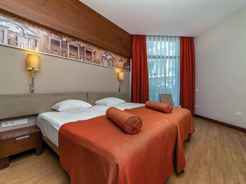 Gezellige hotelkamer met twee eenpersoonsbedden, houten vloer en gordijnen bij het raam.