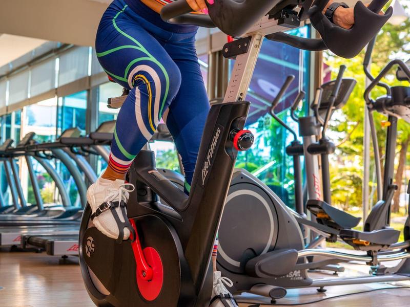 Persoon in kleurrijke legging fietst op een hometrainer in een lichte sportschool.
