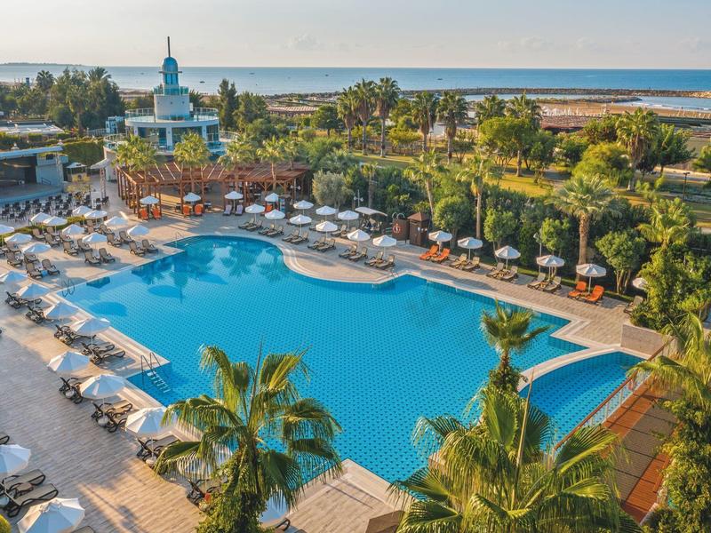Groot buitenzwembad met ligstoelen bij een hotel aan het strand, omgeven door palmbomen.