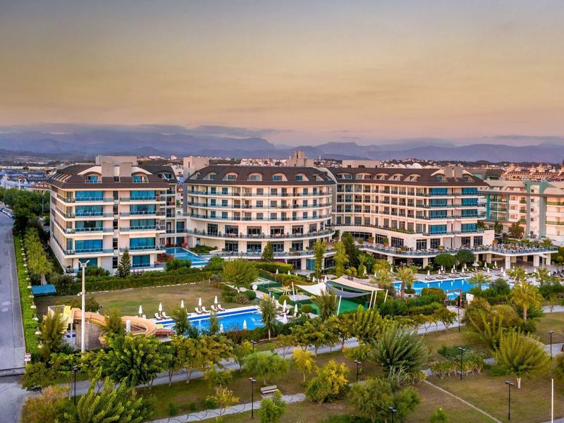 Modern resortcomplex met zwembaden, tuinen en bergzicht bij zonsondergang.