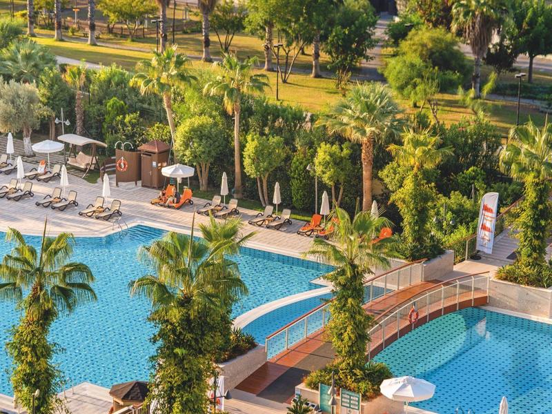 Zwembad met parasols, ligstoelen en weelderige palmbomen in een resortomgeving.