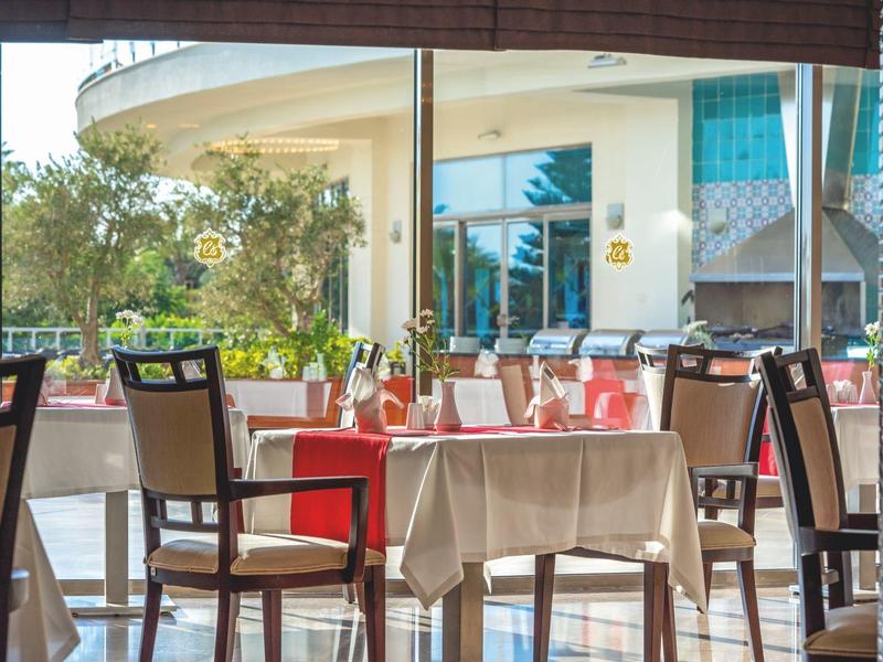 Lichte hotelrestaurant met netjes gedekte tafels en stoelen, grote ramen en groen buiten.
