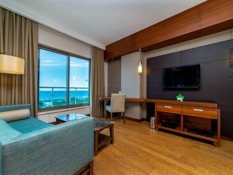 Moderne hotelkamer met zeezicht, houten vloer, bank, bureau en tv.