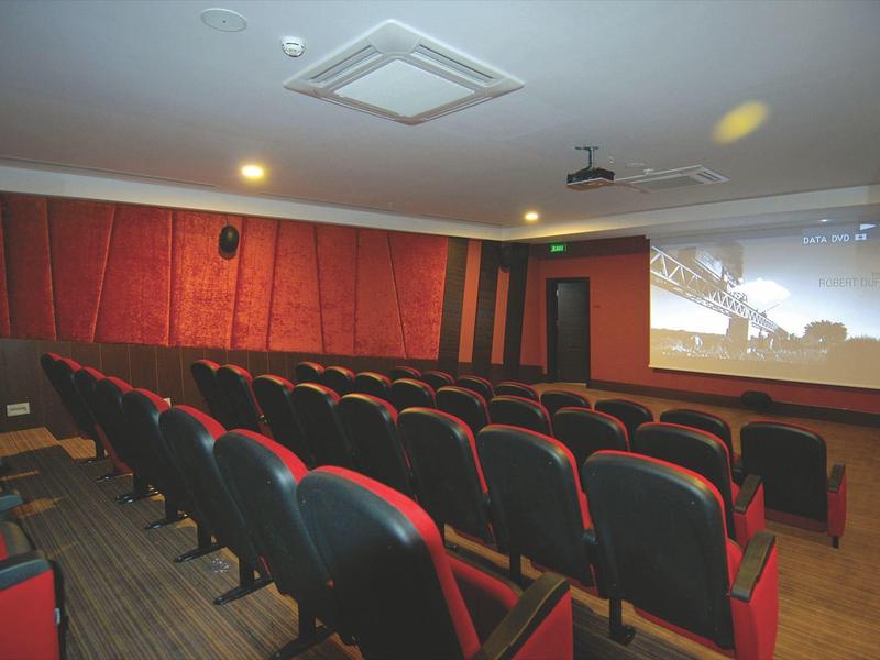 Kleine bioscoopzaal met rijen rood-zwarte stoelen en een groot scherm aan de muur.
