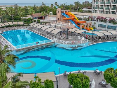 Großer Hotelpoolbereich mit Wasserrutsche, Liegestühlen und umliegender Gartenanlage.